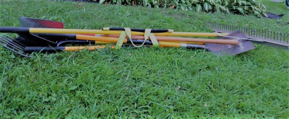 Several long-handled garden tools wrapped and balanced by a single Shovel Sling on grass